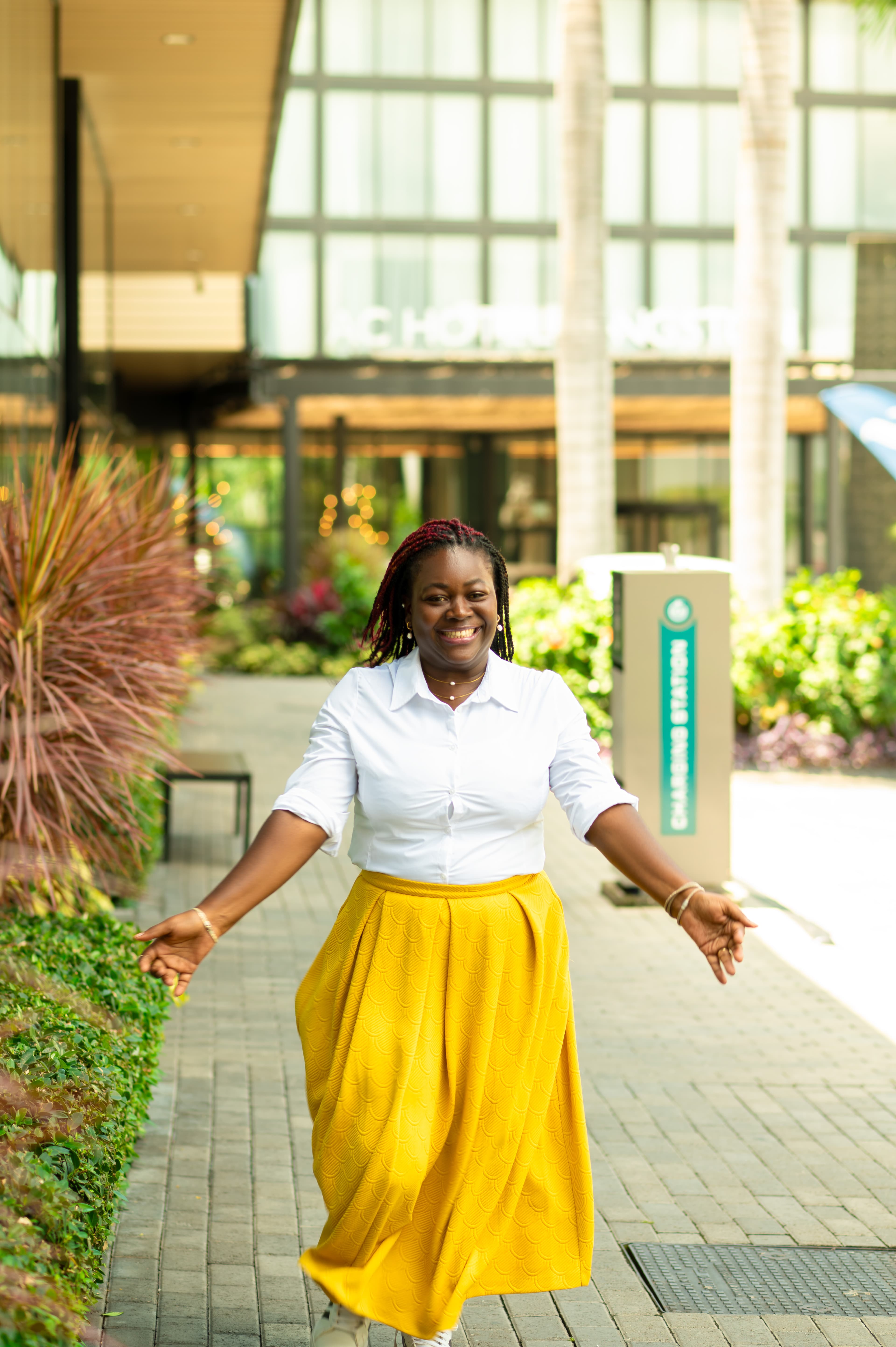 Anwin smiling outdoors in a white shirt and yellow skirt.