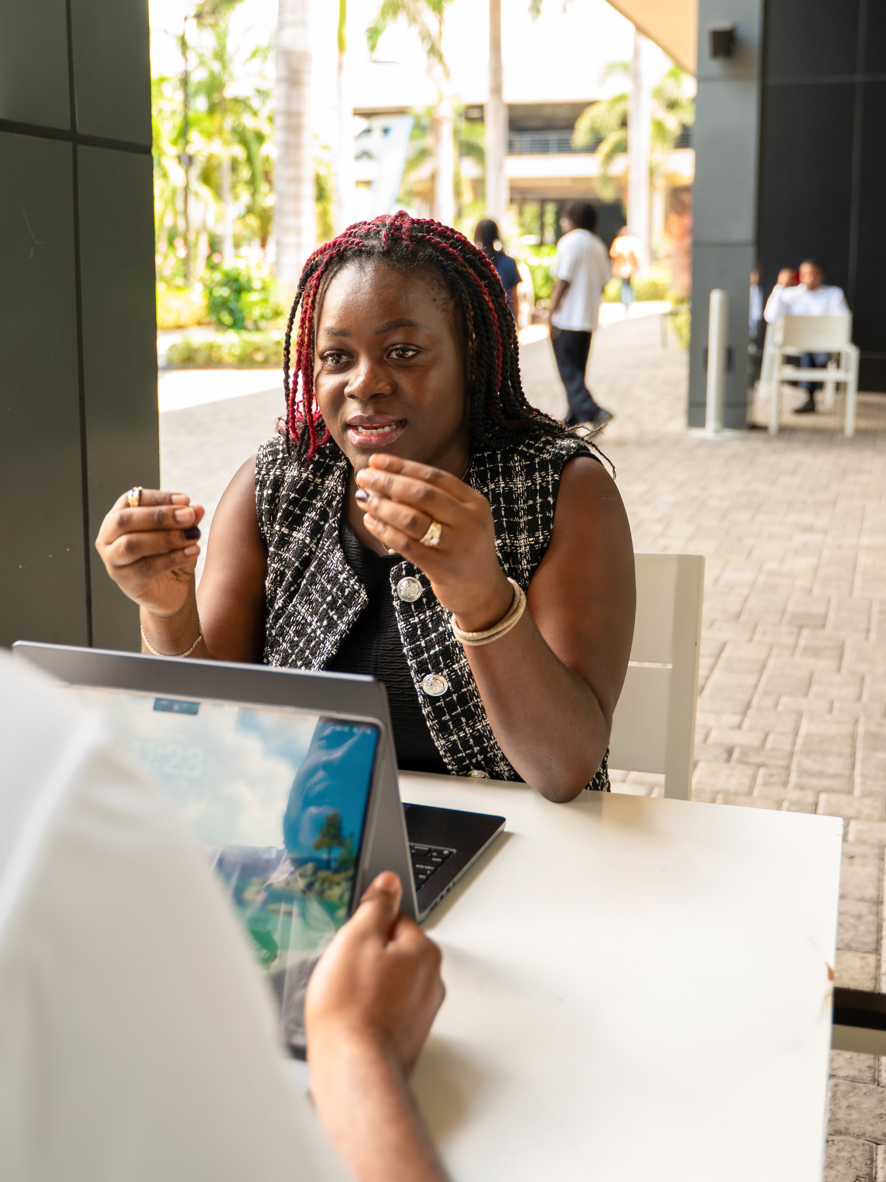 Anwin Mbah in conversation with a client at an outdoor table, working on a laptop